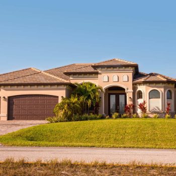 Typical Southwest Florida concrete block and stucco home in the countryside with palm trees, tropical plants and flowers, grass lawn and pine trees. Florida. South Florida single family house